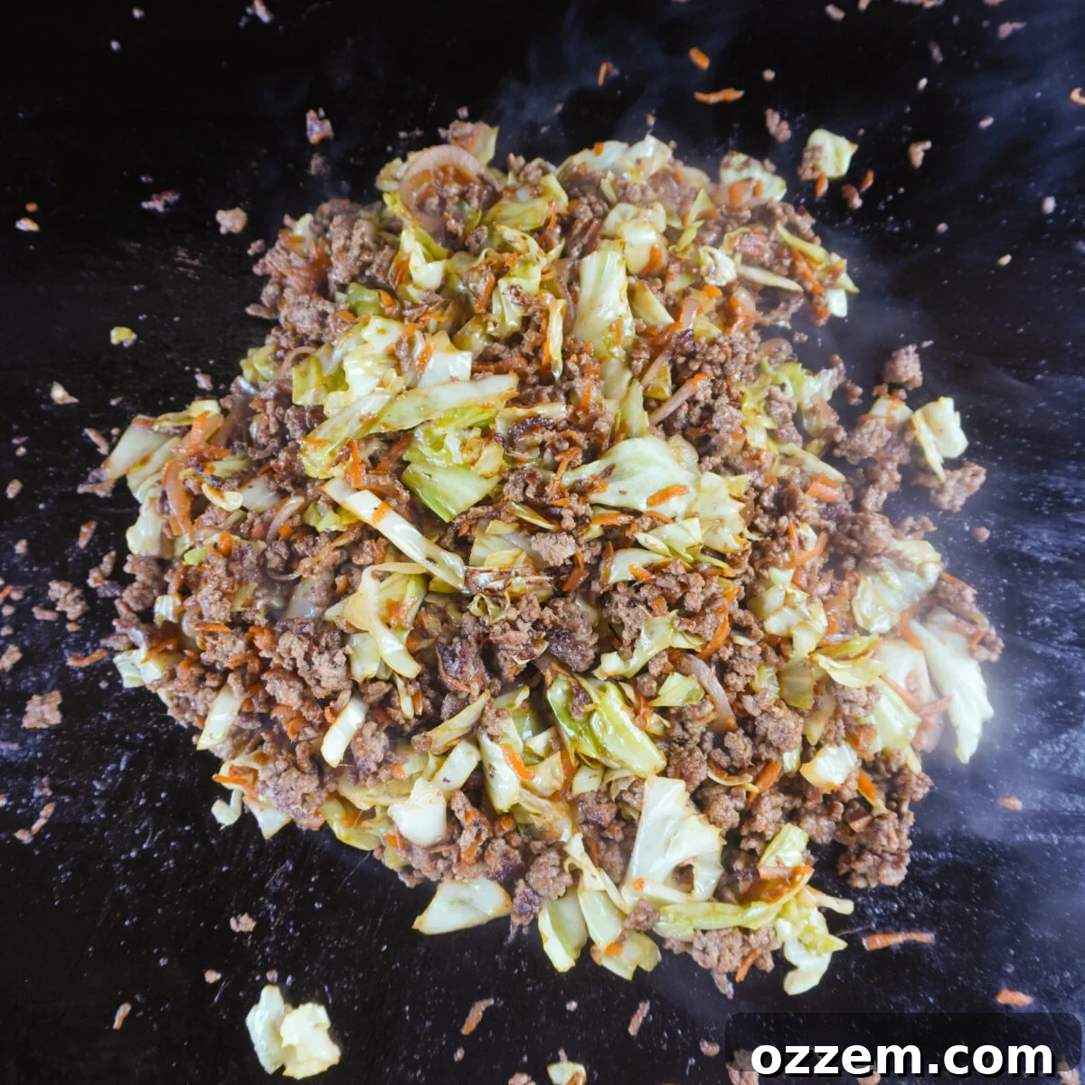 Beef egg roll bowl ingredients mixed on a griddle with sauce being added.