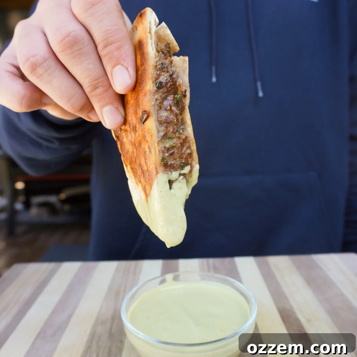 Grilled Beef Arayes sliced in half, revealing the juicy beef filling, and a dipping bowl of creamy avocado cilantro sauce.
