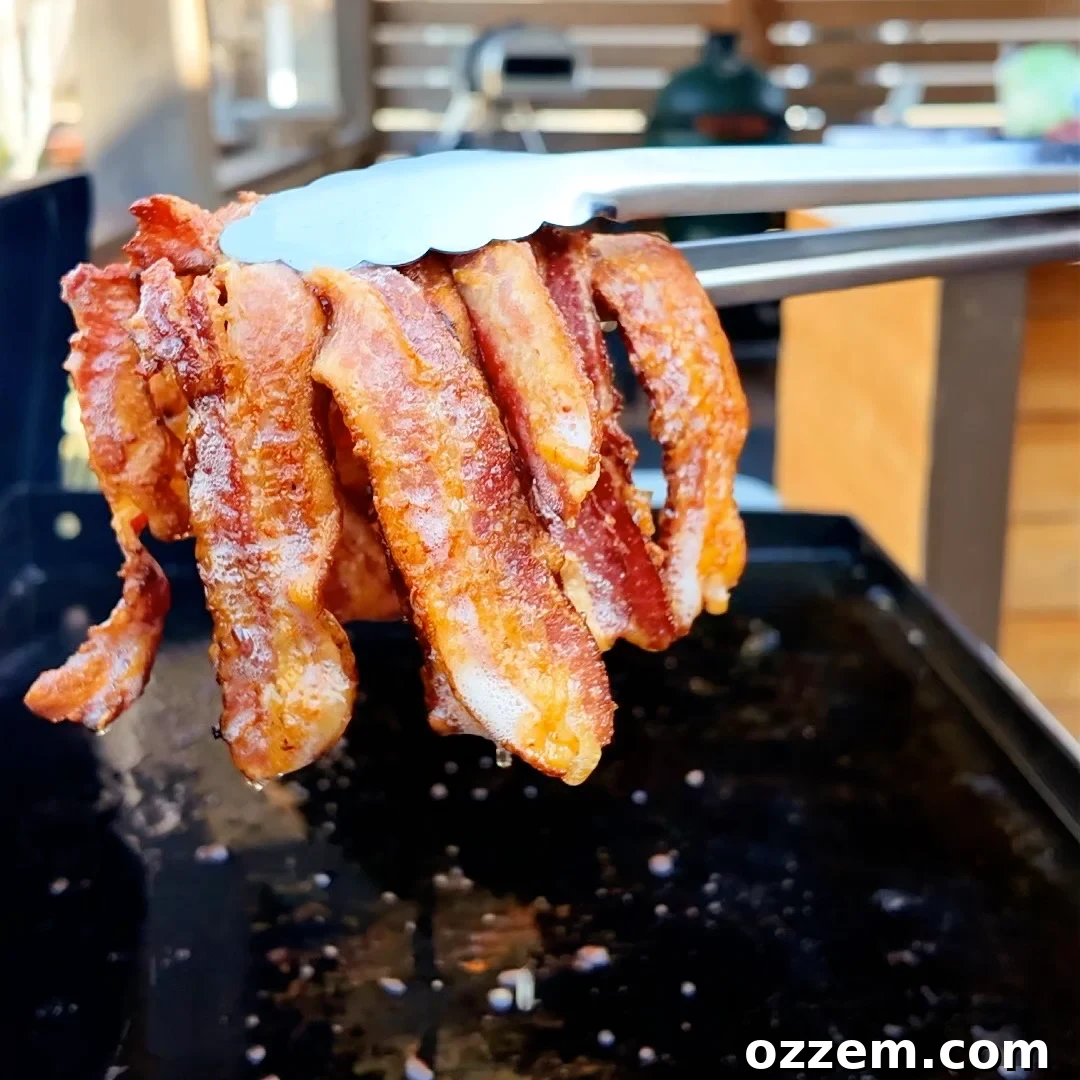 Crispy bacon sizzling on a griddle, ready to be removed with tongs.