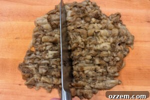 Chopping the flesh of roasted eggplants on a wooden cutting board.