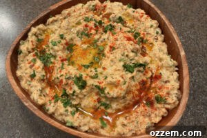 Wooden bowl filled with baba ganoush and topped with olive oil drizzle, chopped parsley, and a dusting of paprika.
