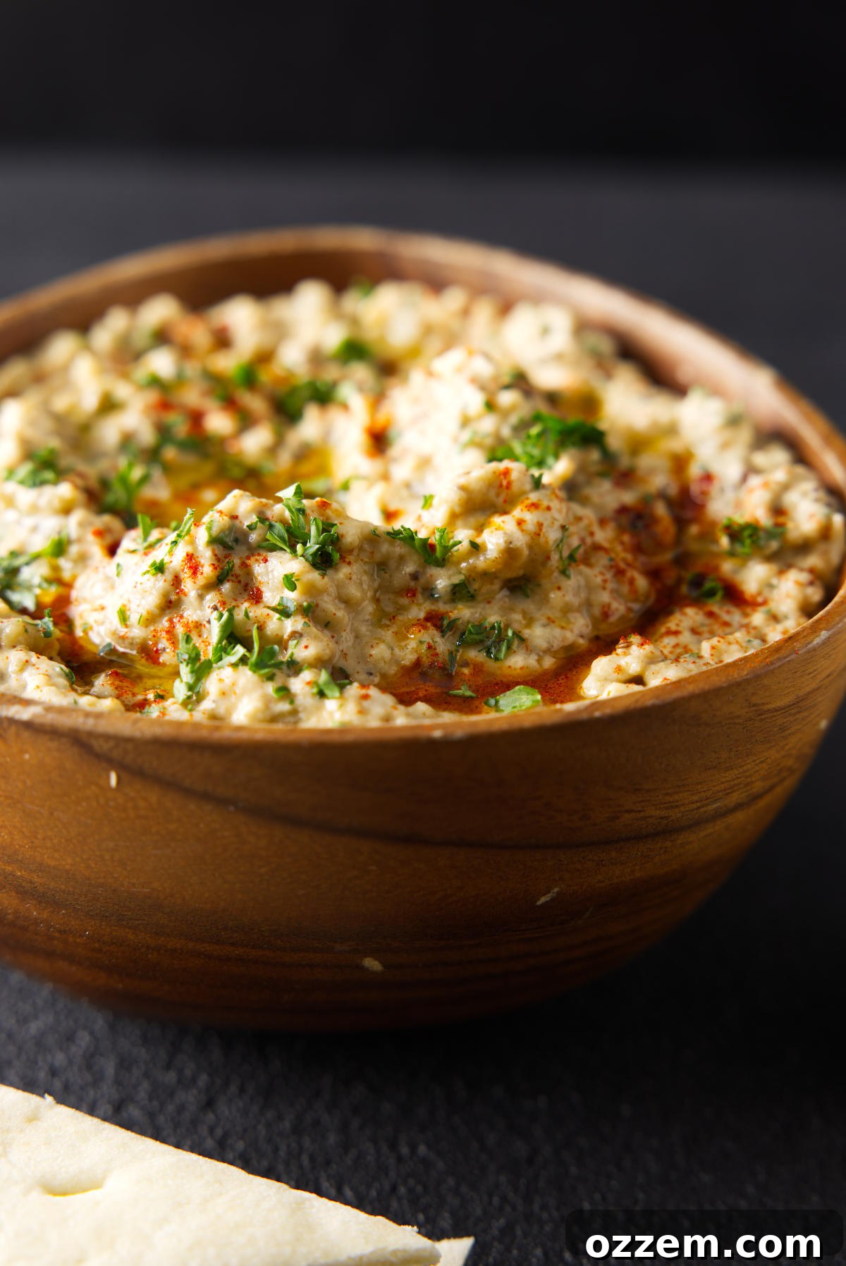 Smoked Baba Ganoush in a wooden bowl topped with chopped parsley and olive oil, viewed from a slightly elevated angle.
