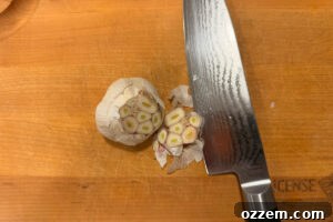 Cutting the top off of a bulb of garlic on a wooden cutting board.