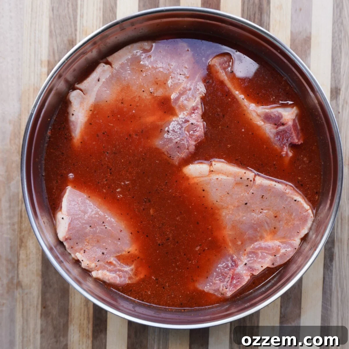 apple juice and cider vinegar brine with raw pork chops marinating inside bowl.