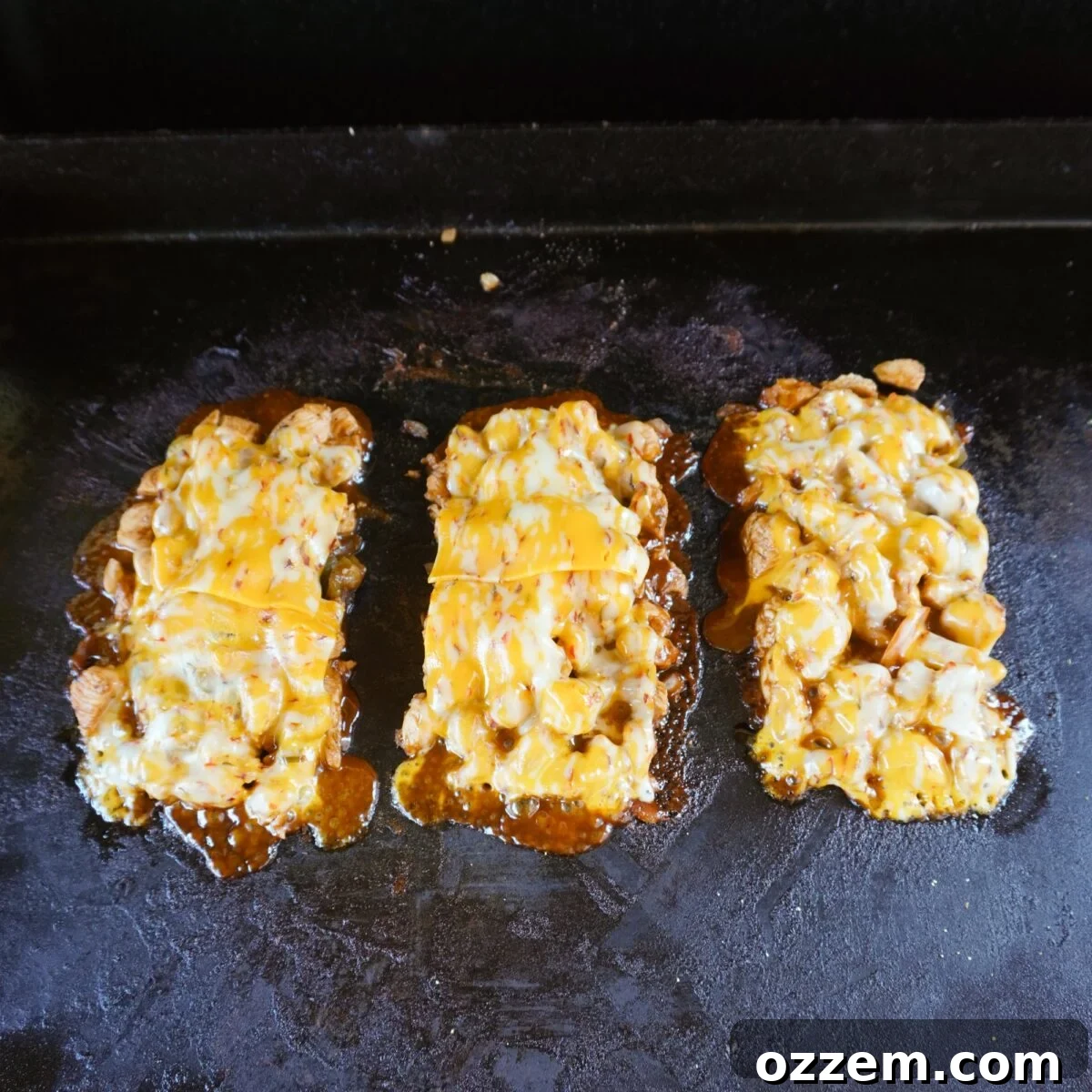 individual servings of grilled chicken with melted cheese on griddle surface.