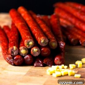 Smoked jalapeño cheddar venison snack sticks stacked in a pile on a butcher block.
