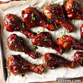 Several BBQ smoked chicken drumsticks coated in bbq sauce on parchment paper.
