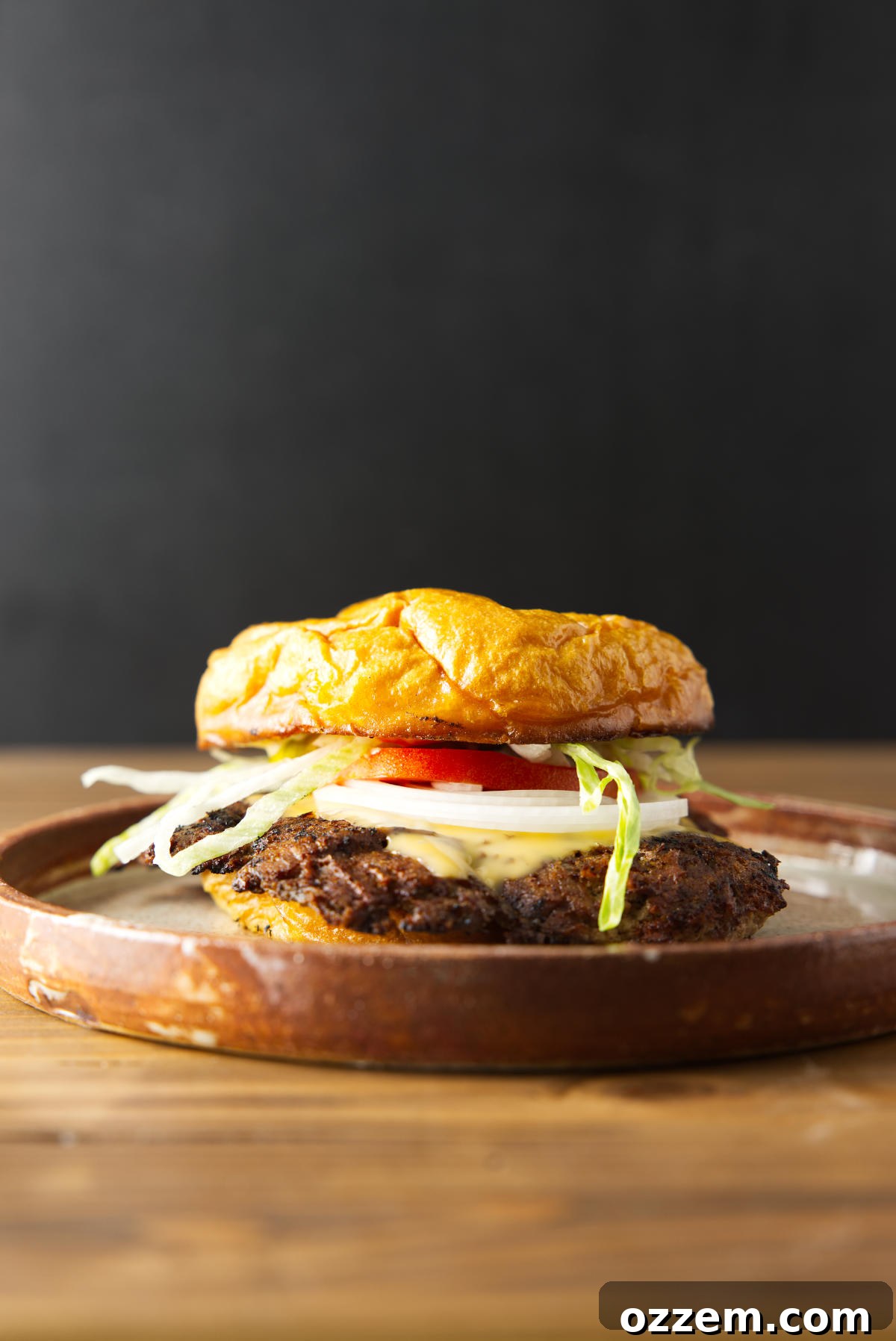Blackstone Smash Burgers with Perfectly Crispy Edges 2 Blackstone smash burger loaded with toppings and smash burger sauce plated on a brown ceramic dish.