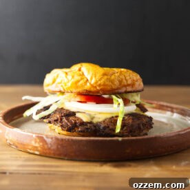 Smash burger with melty cheese, onion, tomato, and lettuce plated on a brown ceramic plate.