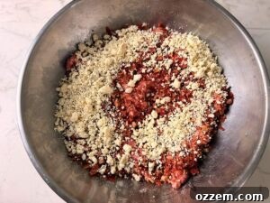 Sprinkling gorgonzola cheese over meat in a stainless steel bowl.