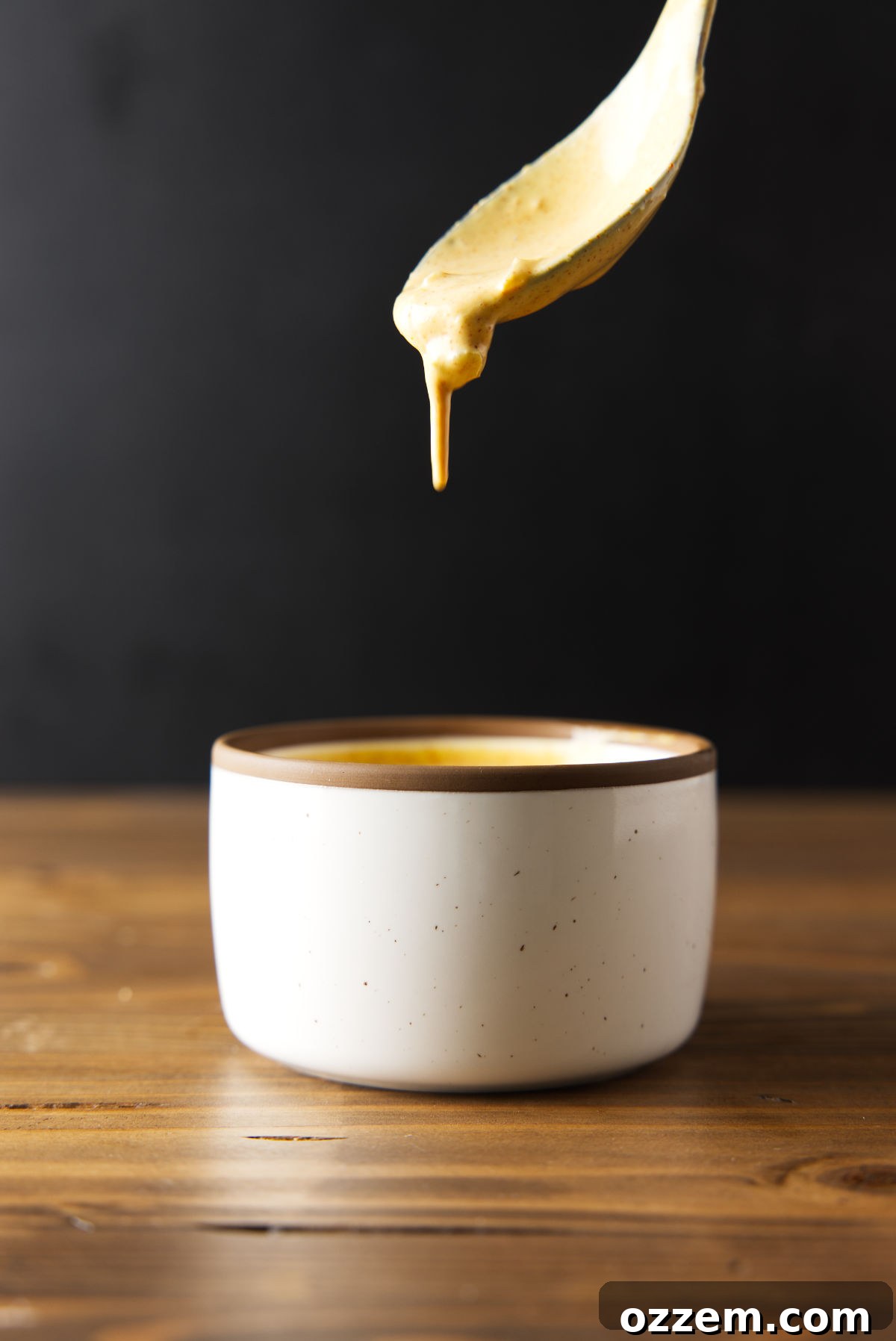 Smash burger sauce dripping from a spoon in to a bowl on a wood cutting board.
