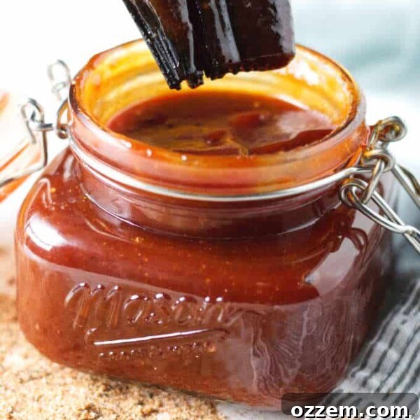 Kansas City-style BBQ sauce in a mason jar sitting on gray and white napkin with some loose seasoning on the table in front