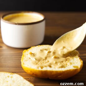 Burger sauce spreading on burger bun using a spoon on a wooden counter.