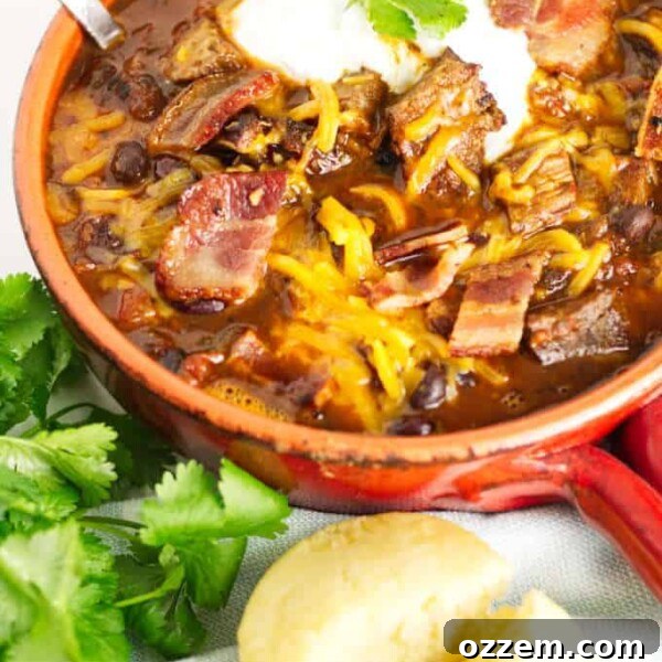 small red pot filled with brisket chili with cheese and sour cream and a garnish of cilantro, cornbread muffin in the foreground