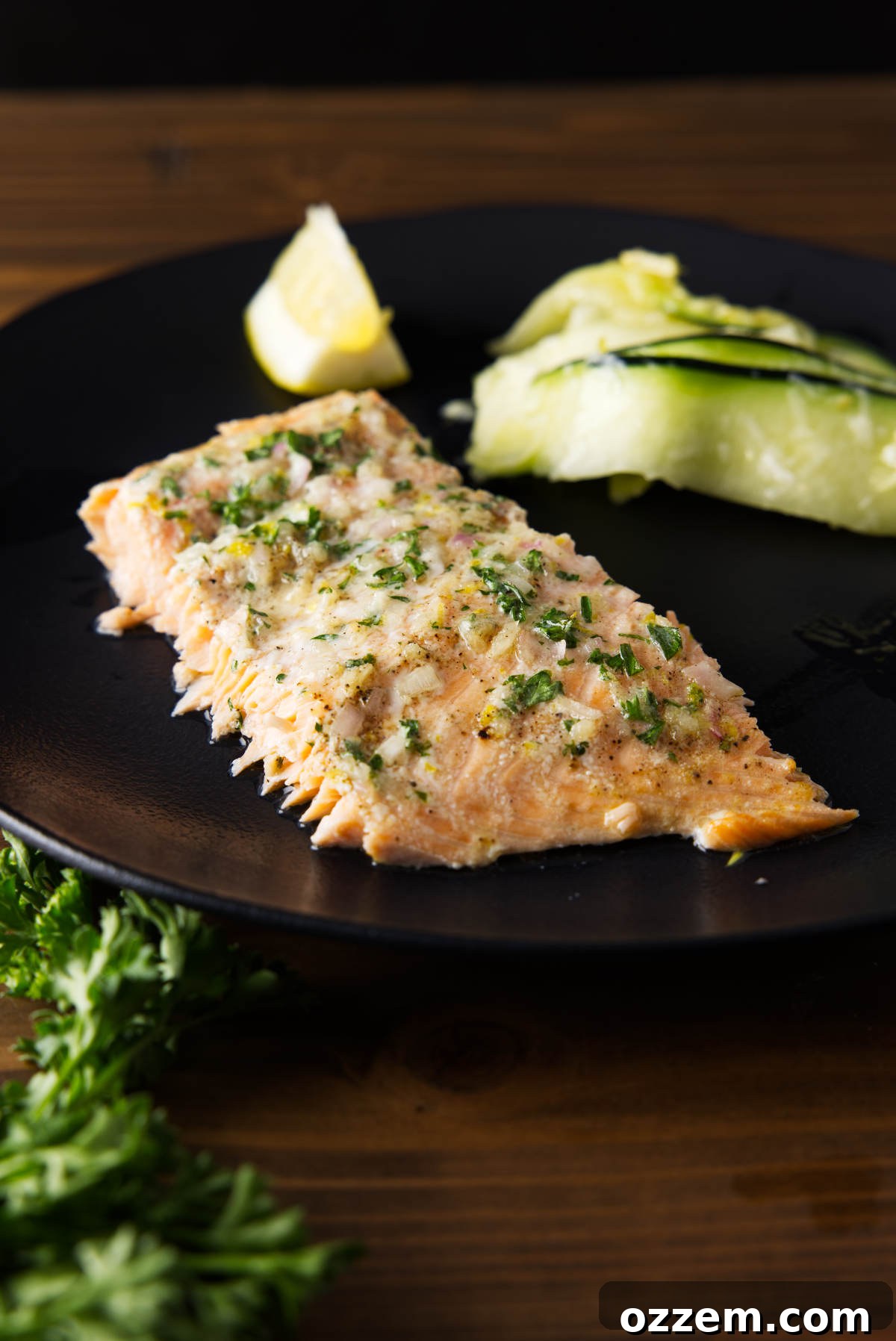 Smoky Pellet Grill Salmon Recipe 6 Slice of salmon with compound butter on top served on a black plate with a lemon wedge and zucchini salad.