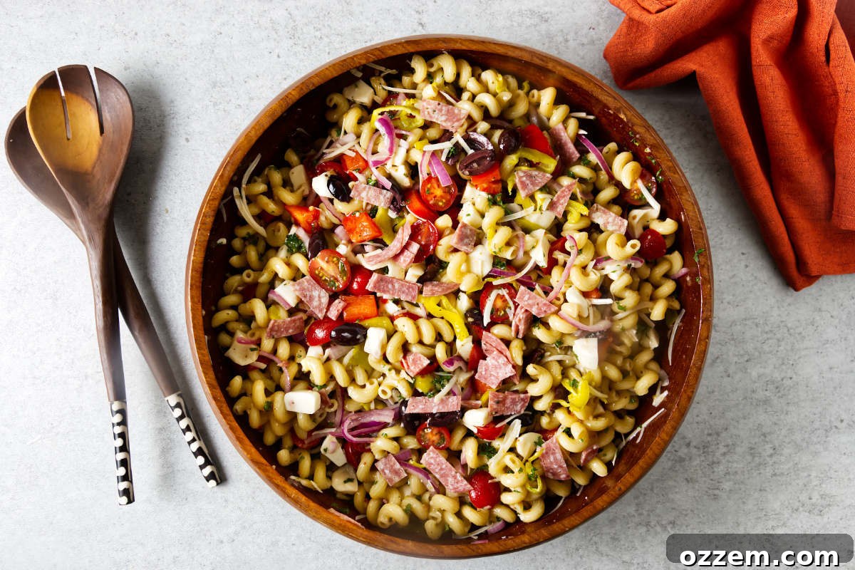 A wooden salad bowl filled with Italian pasta salad next to salad utensils.