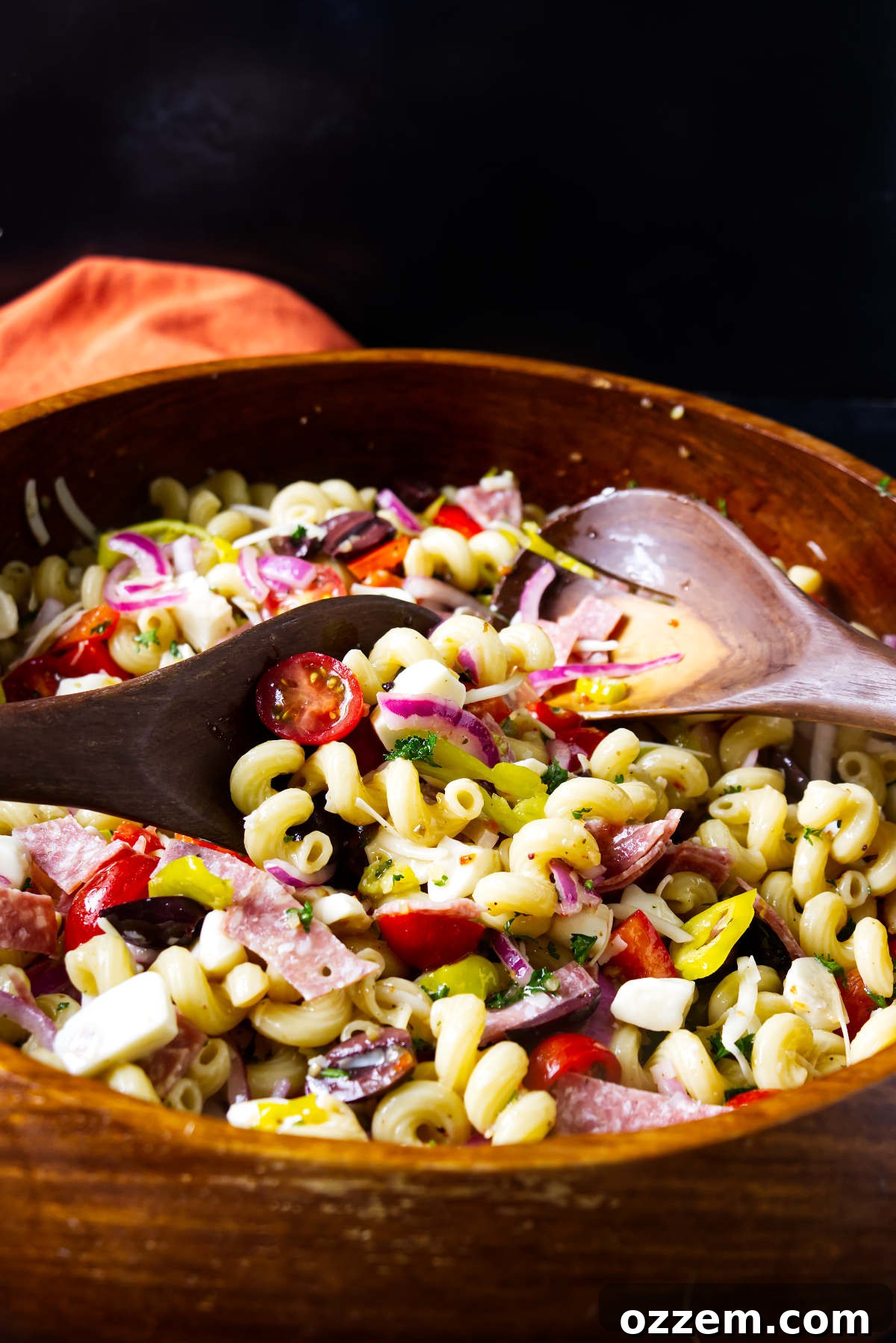 Tossing Italian pasta salad with large wooden utensils.