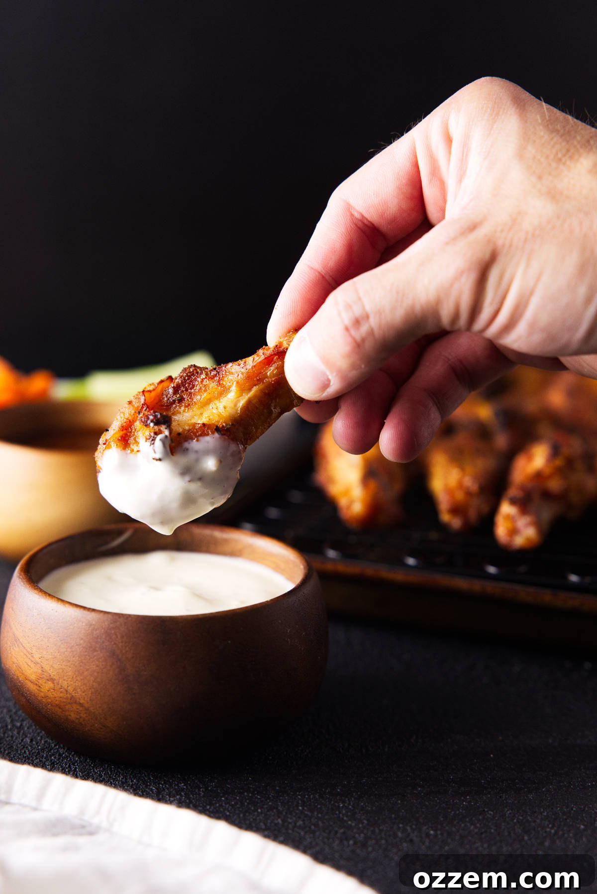 Dipping smoked chicken wing in blue cheese from a wooden bowl.