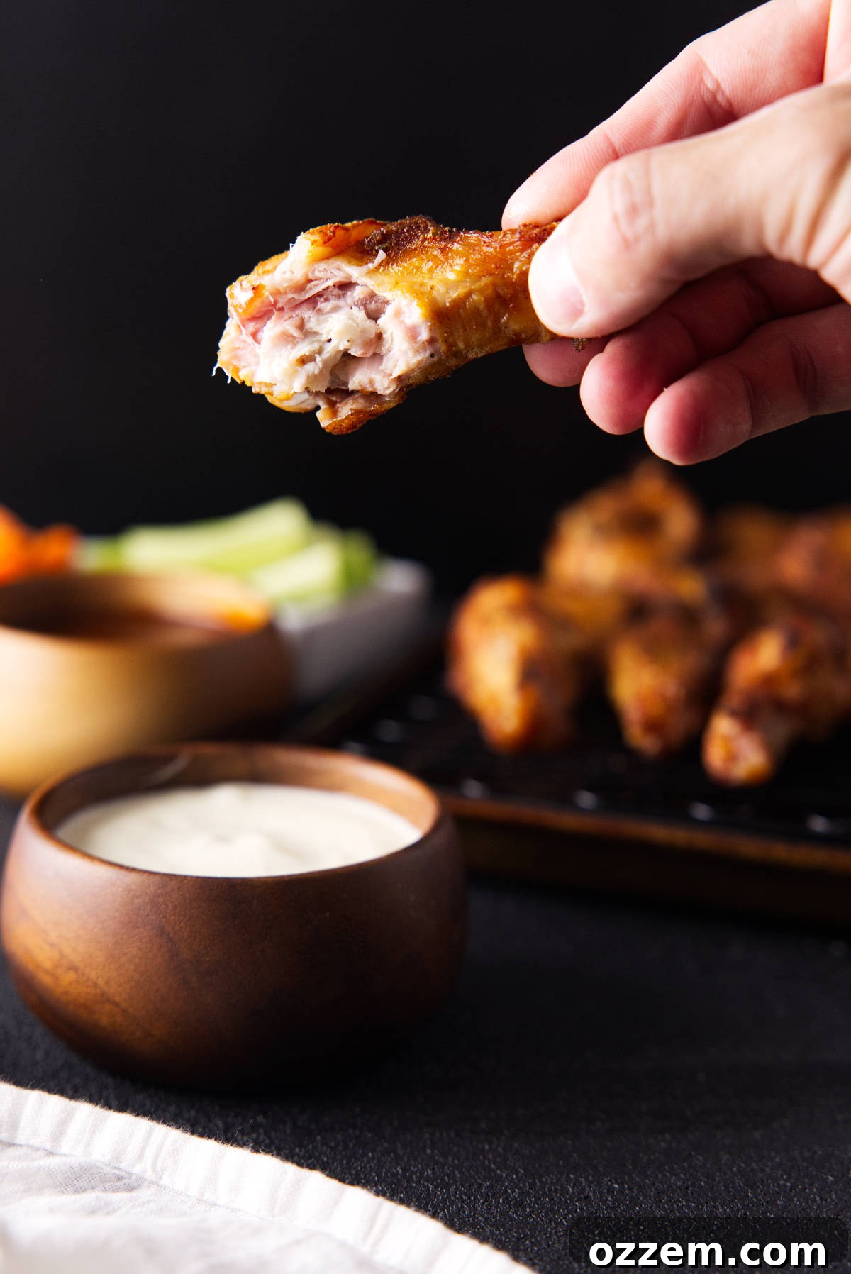 Hand holding a smoked chicken wing with a bite taken out of it.