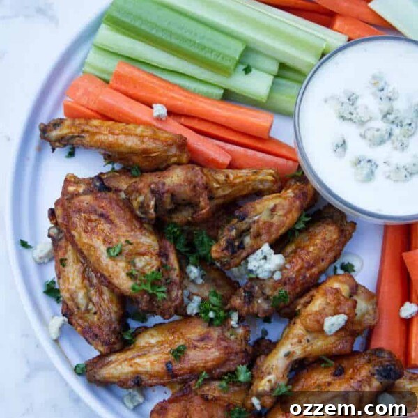 chicken wings with buffalo sauce sitting on a white plate with blue cheese and celery and carrots in the background