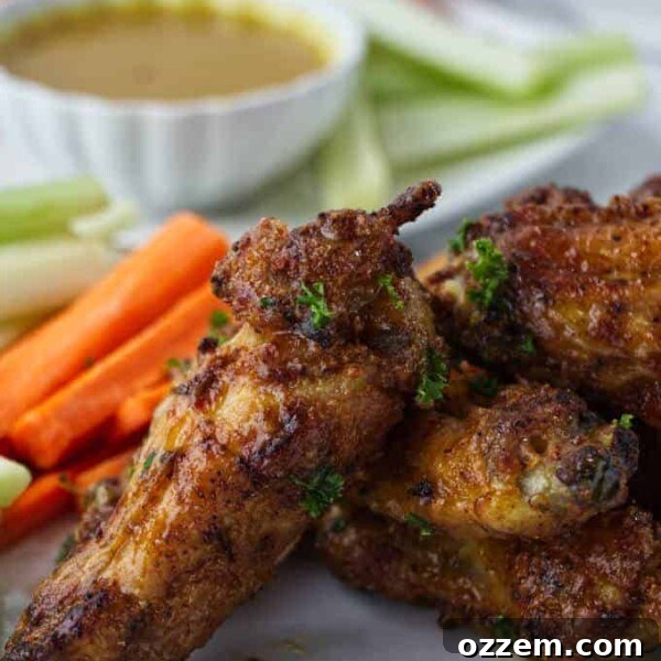 crispy air fried chicken wings sitting on a white plate with sliced carrots and celery with parsley sprinkled on top and dish of honey mustard in background