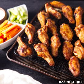 Square image of smoked chicken wings with carrots and celery sticks.