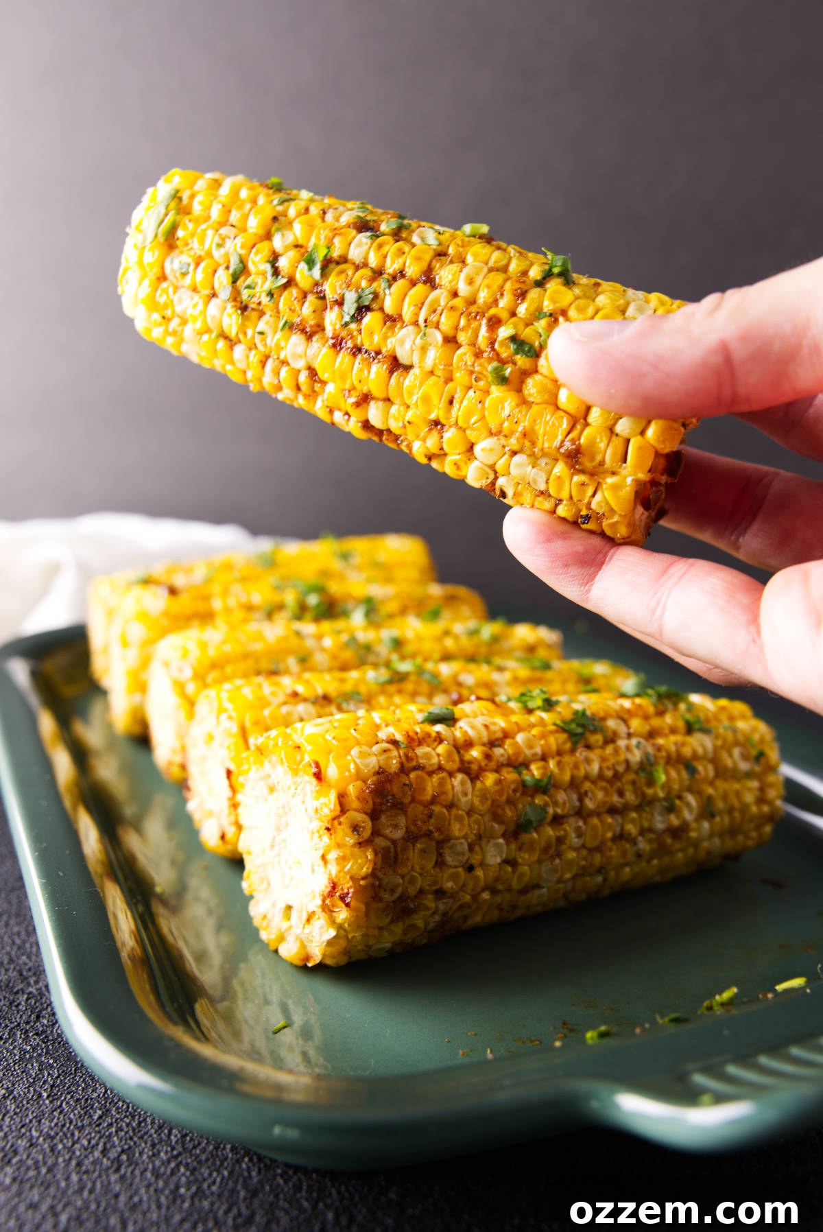Hand holding pellet grill smoked corn on the cob brushed with barbecue butter.