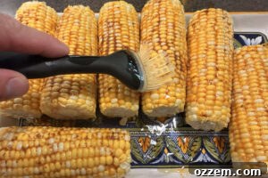 Brushing corn on the cob with smoky barbecue butter before smoking.