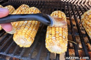 Basting smoked corn on the cob with barbecue butter on the pellet grill.