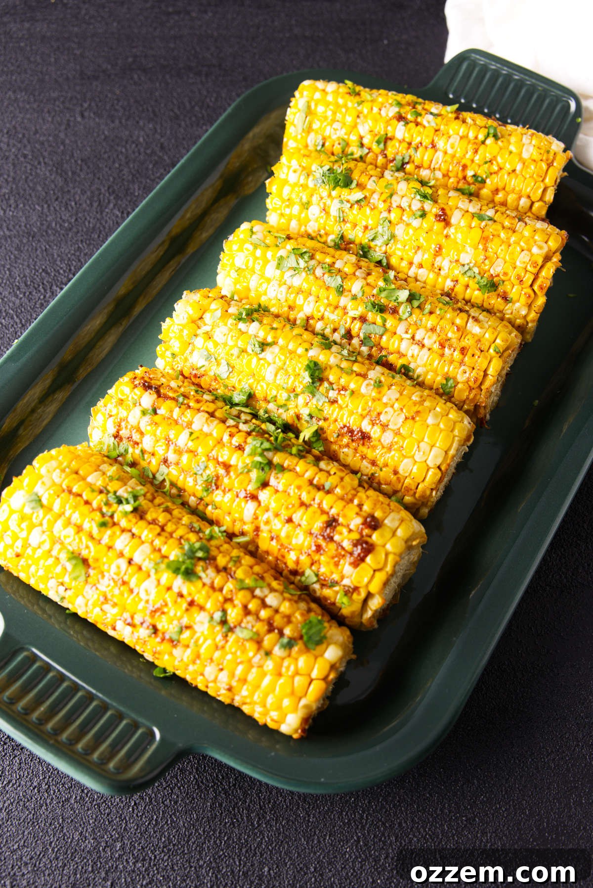Smoked corn on the cob on a platter with barbecue seasoning and herbs.