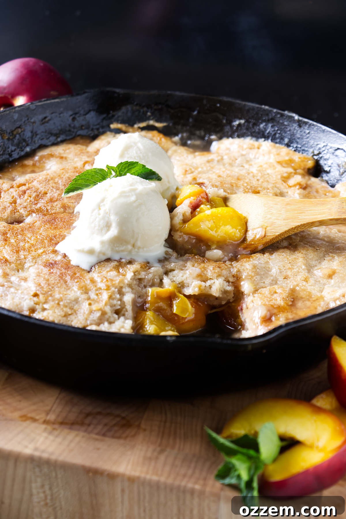 Scooping smoked peach cobbler from a cast iron skillet.