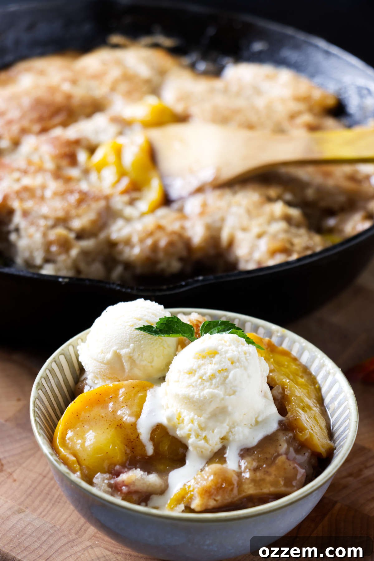 A bowl of pellet grill peach cobbler next to a cast iron skillet.