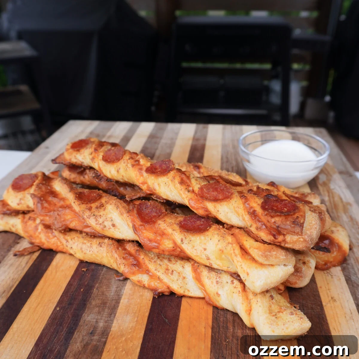 Homemade Cheesy Pizza Twist Sticks 2 Pizza Stick Twists presented on a cutting board with a bowl of ranch dipping sauce.